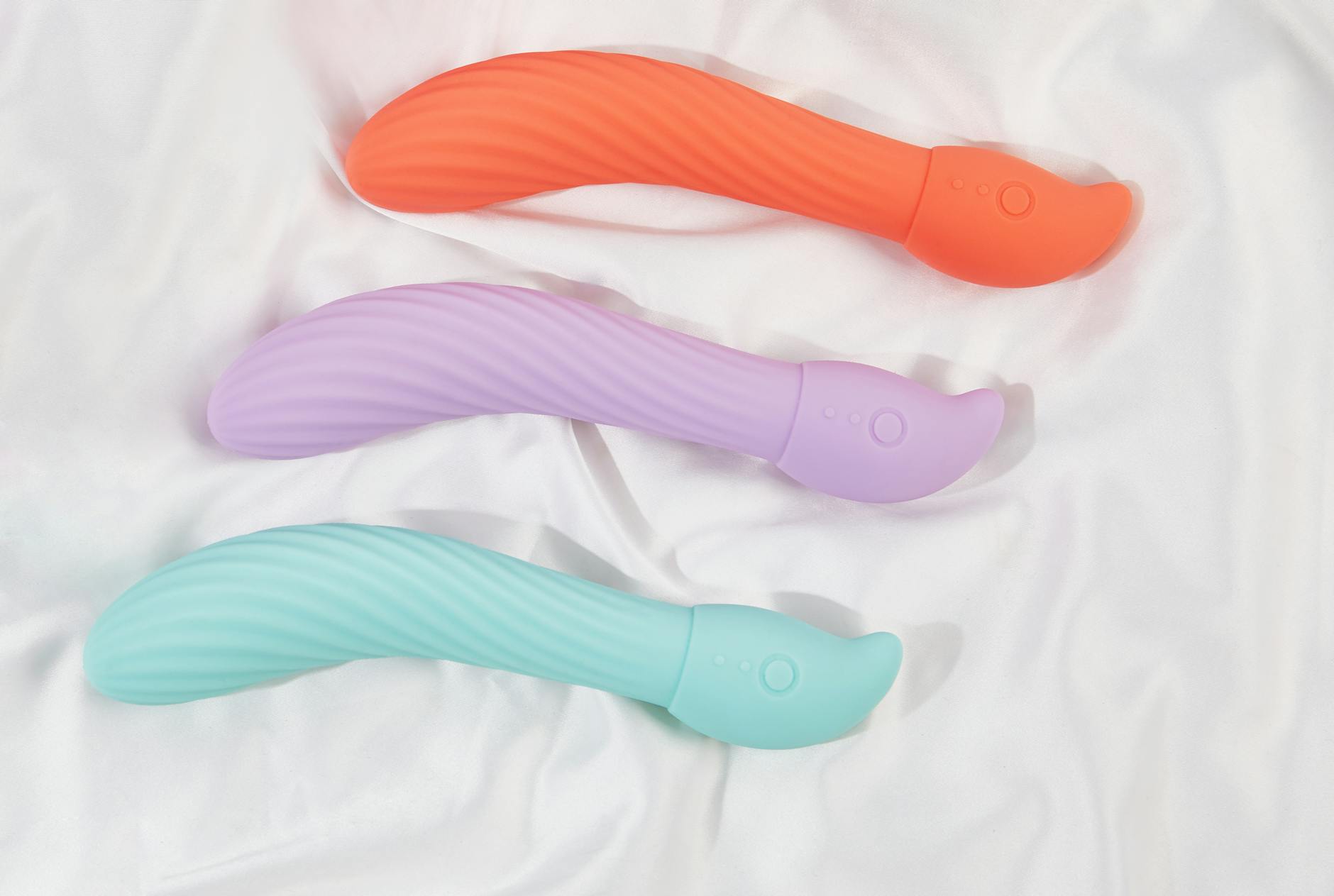 Three colorful clitoral vibrators arranged on white fabric, highlighting their smooth texture and design variety