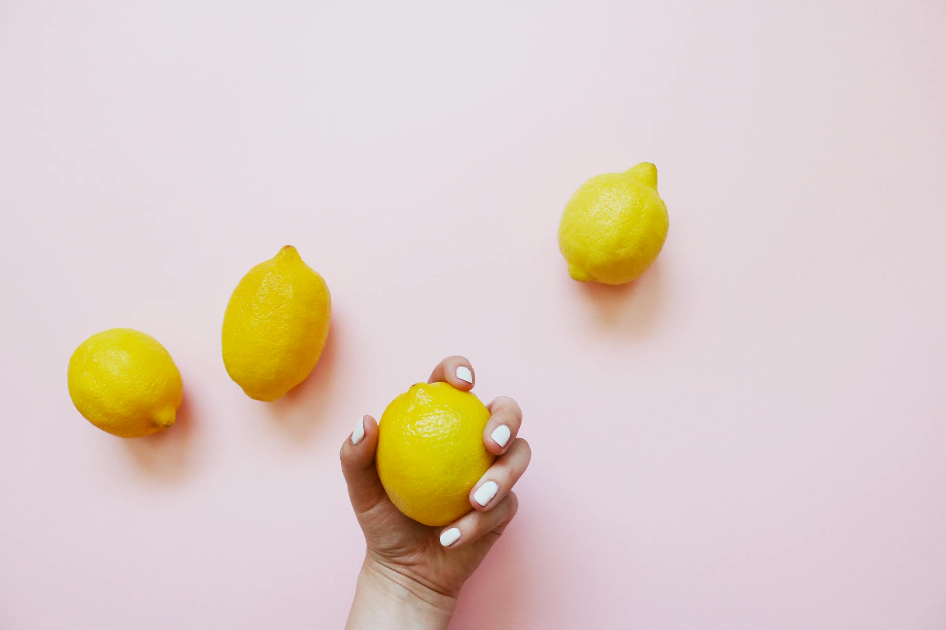 A hand holding a fresh lemon on a soft pink background, symbolizing heightened sensitivity and natural pleasure.