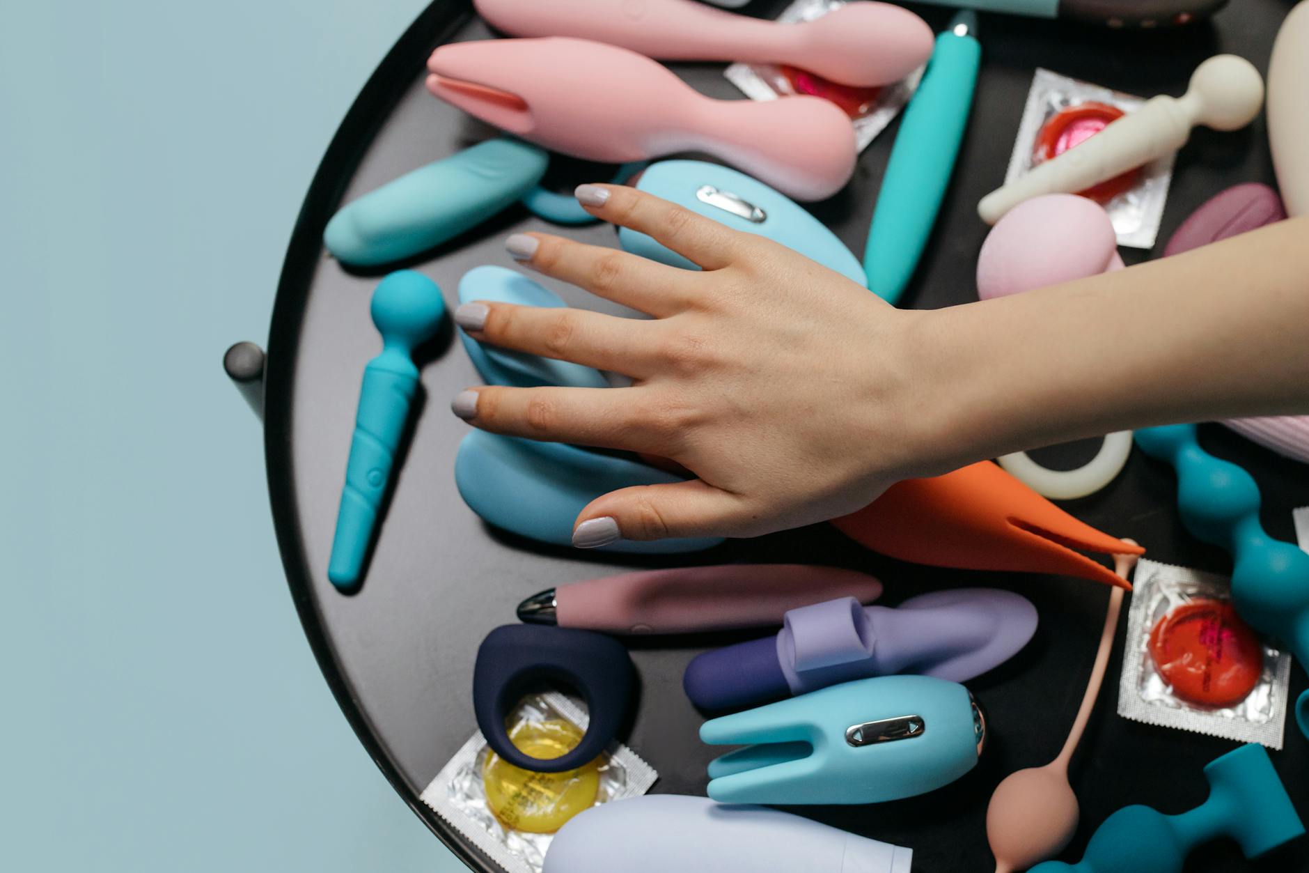 A hand reaching over a collection of colorful lemon vibrators and sex toys on a table