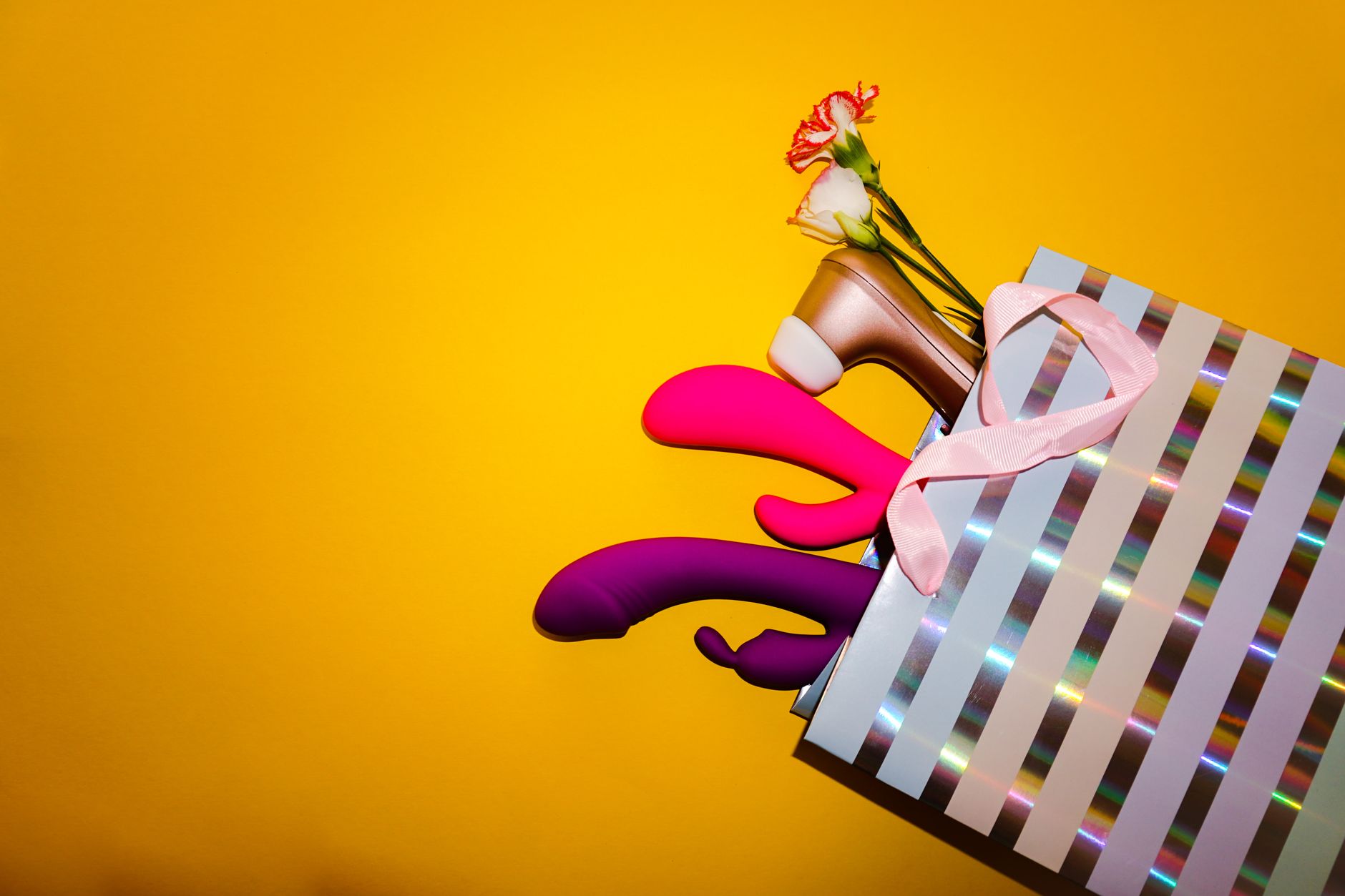 Vibrant collection of colorful lemon vibrators and clitoral toys displayed with flowers and greenery against a bright yellow background.